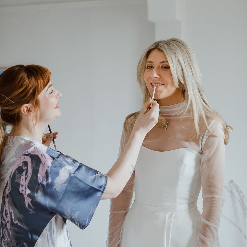 Bride in strapless wedding dress with mesh overlay top getting lipstick put on 