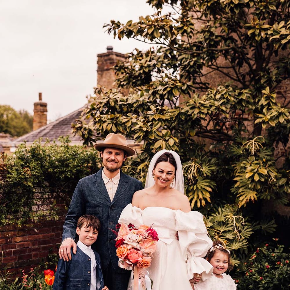 The bride and groom pose with their two children at their outdoor summer wedding 