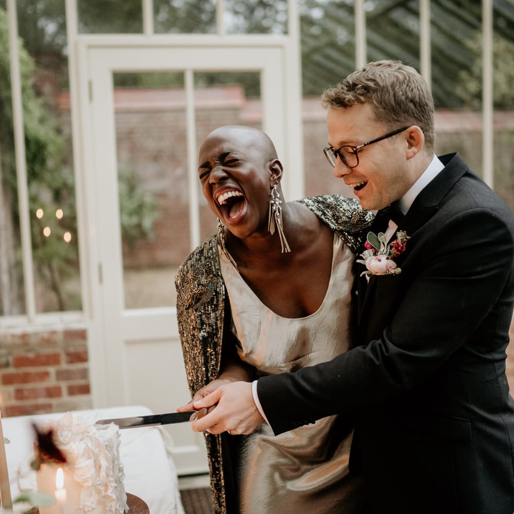 Bride and groom laughing whilst cutting their wedding cake at their intimate Our Beautiful Glasshouse elopement 