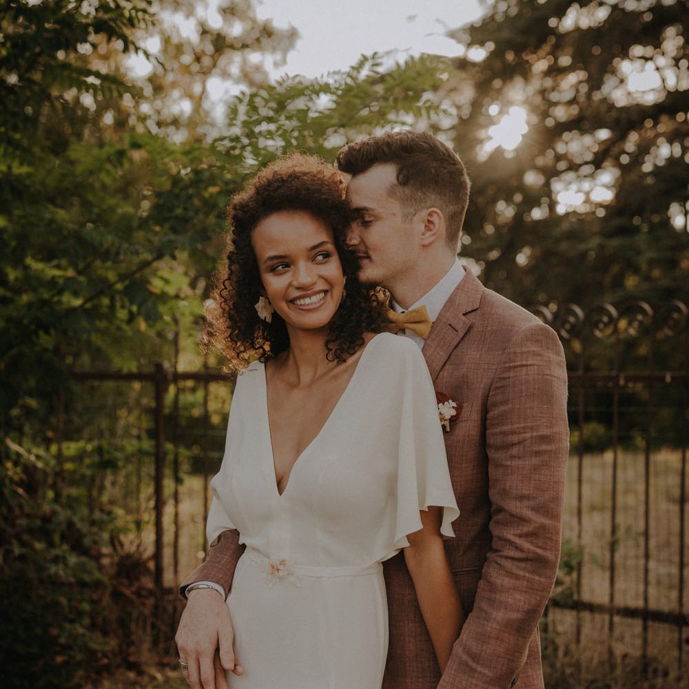 Groom in a brown wedding suit nuzzling his brides naturally curly hair 