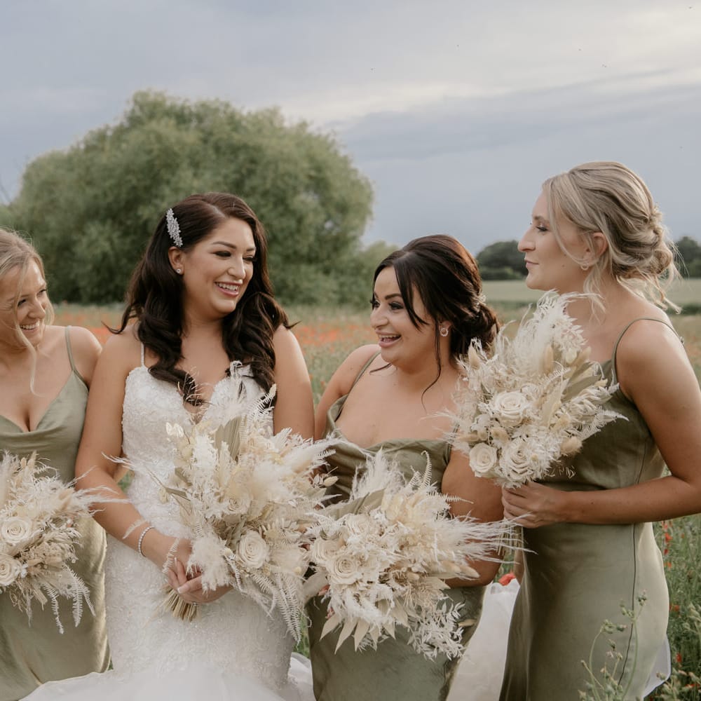 Bride and bridesmaids standing in a poppy field holding dried flower bouquets 