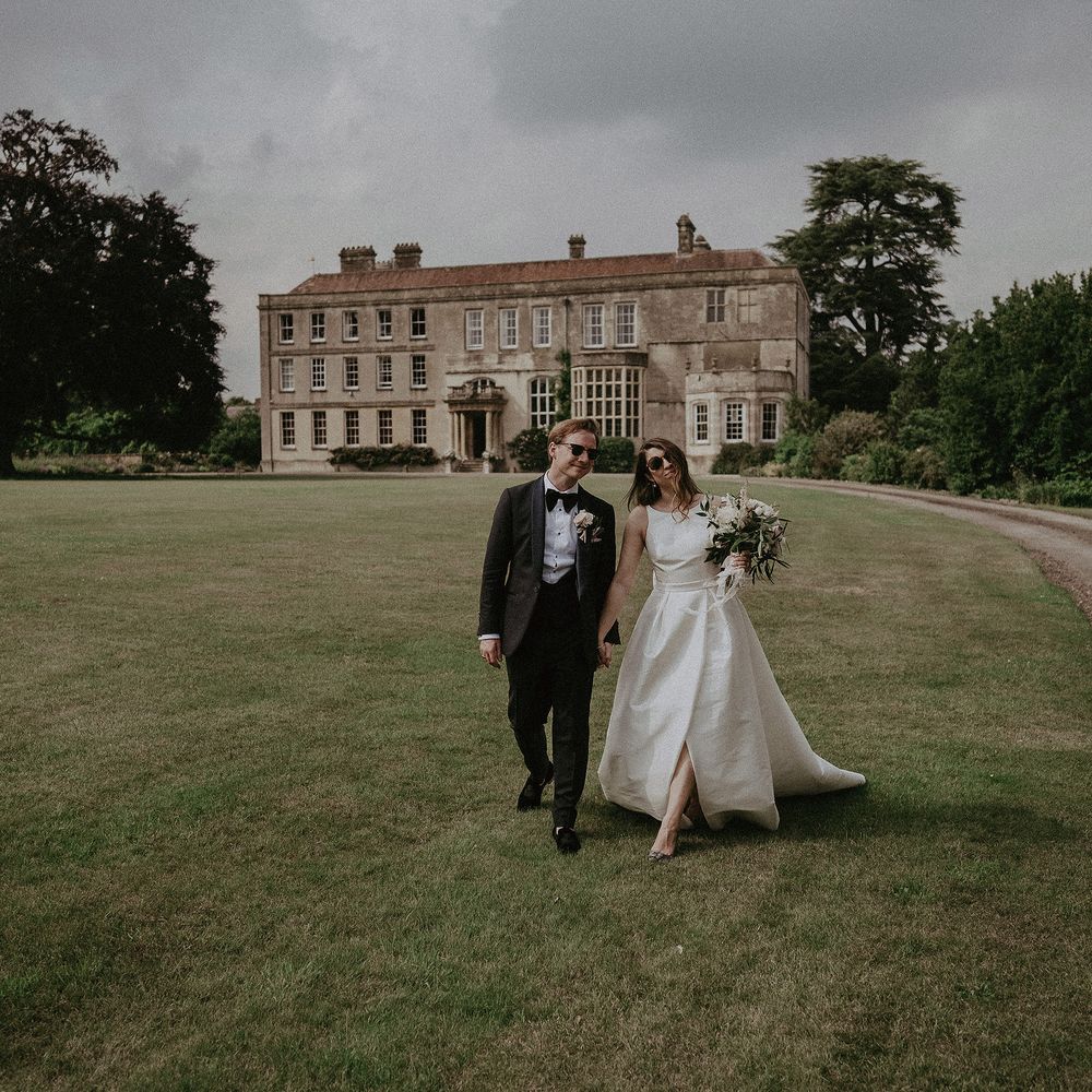 Bride & groom walk through the grounds of Elmore Court whilst wearing sunglasses on their wedding day
