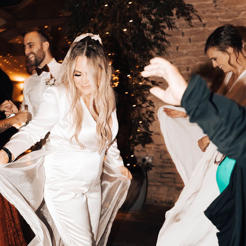 Blonde bride dances during reception whilst wearing bridal jumpsuit and veil