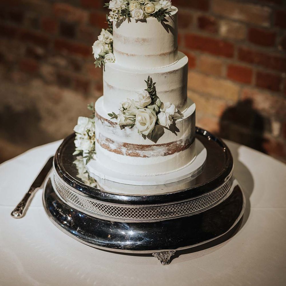 Three tier semi naked wedding cake with white frosting and white rose decoration