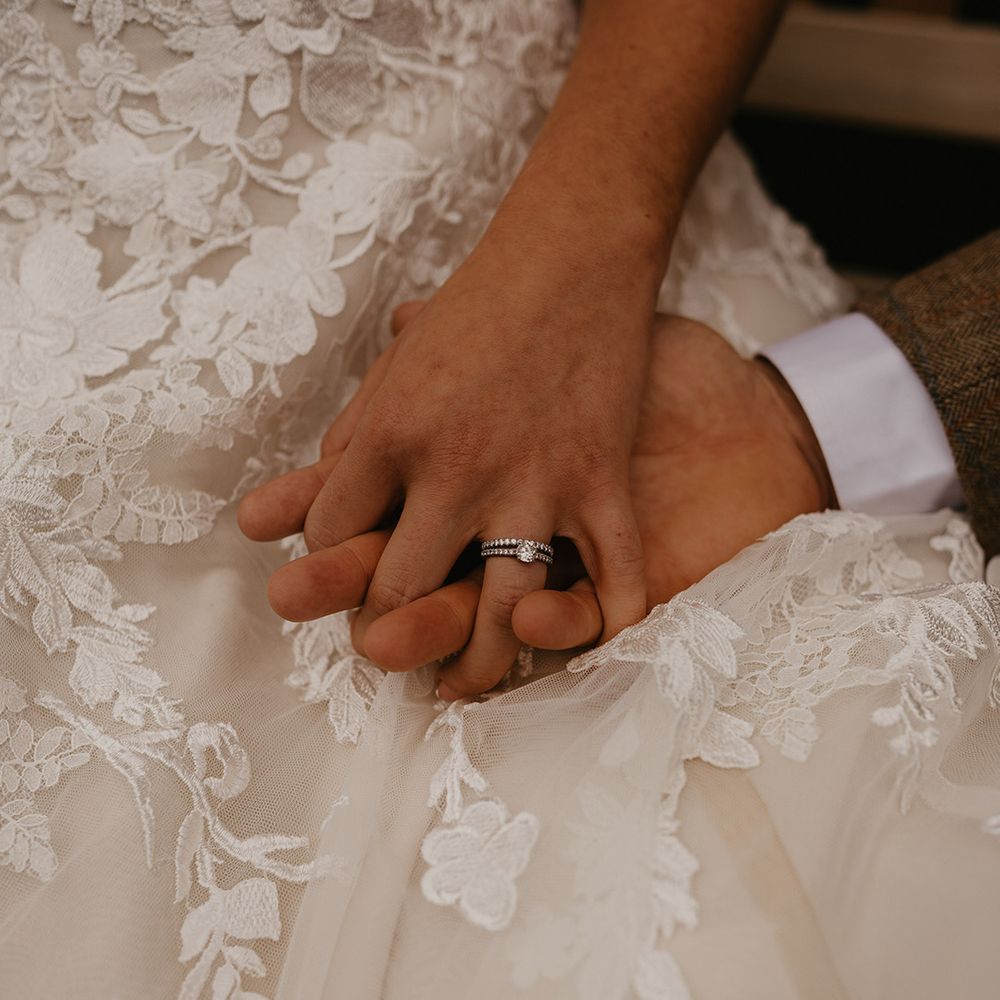 Bride with silver engagement ring and wedding band intertwines fingers with the groom