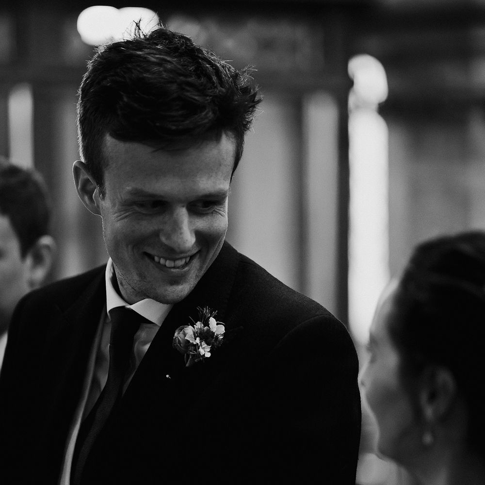 Groom with white flower buttonhole smiles brightly at the bride 