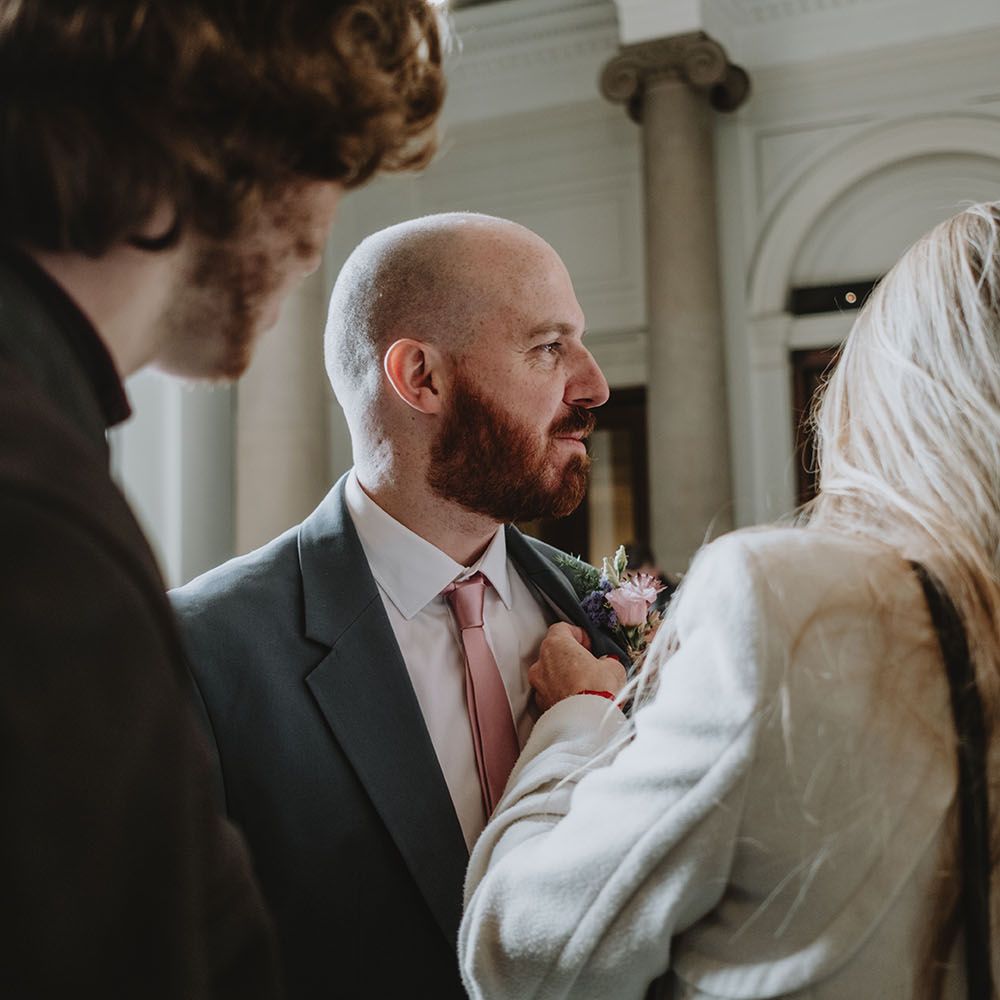 Groom wears grey high street suit with silk pale pink tie and matching floral buttonhole 