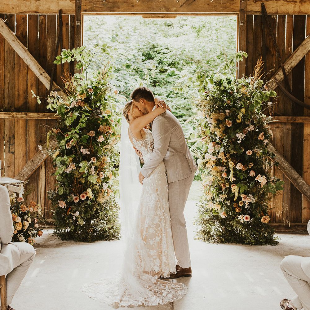 Bride and groom share their first kiss as a married couple in front of the flower column altar decorations at Nancarrow Farm