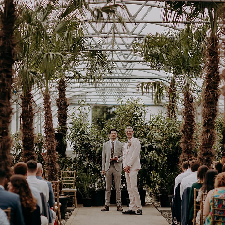 Groom waits at the bottom of the palm tree lined aisle for Bride