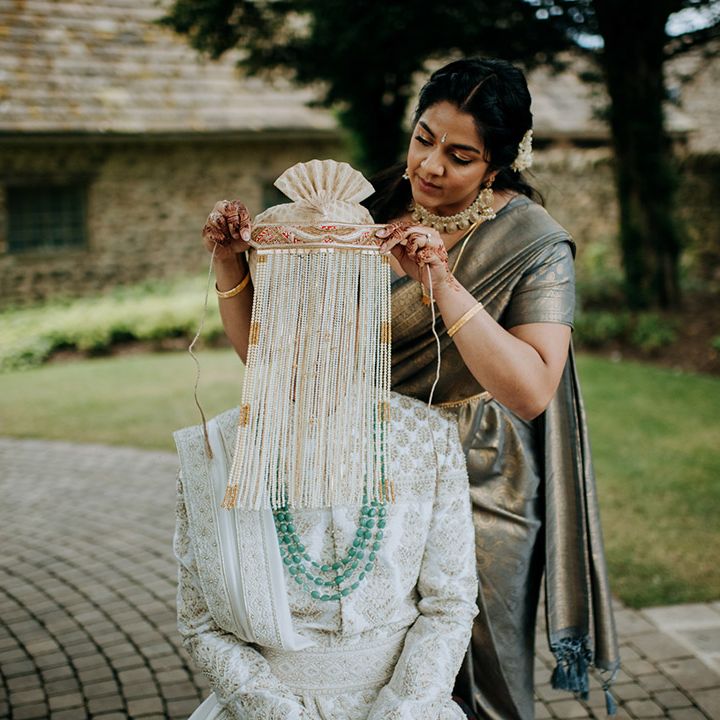 Groom wears embellished sherwani and has his face covered with beads before wedding ceremony outdoors