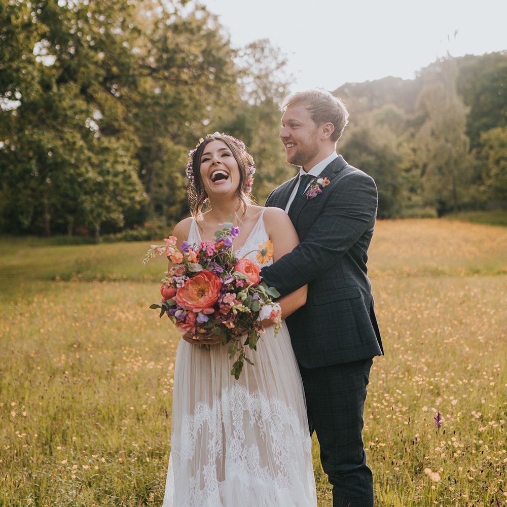 Bride holds colourful floral bouquet filled with peonies as she stands with her groom during golden hour portraits 