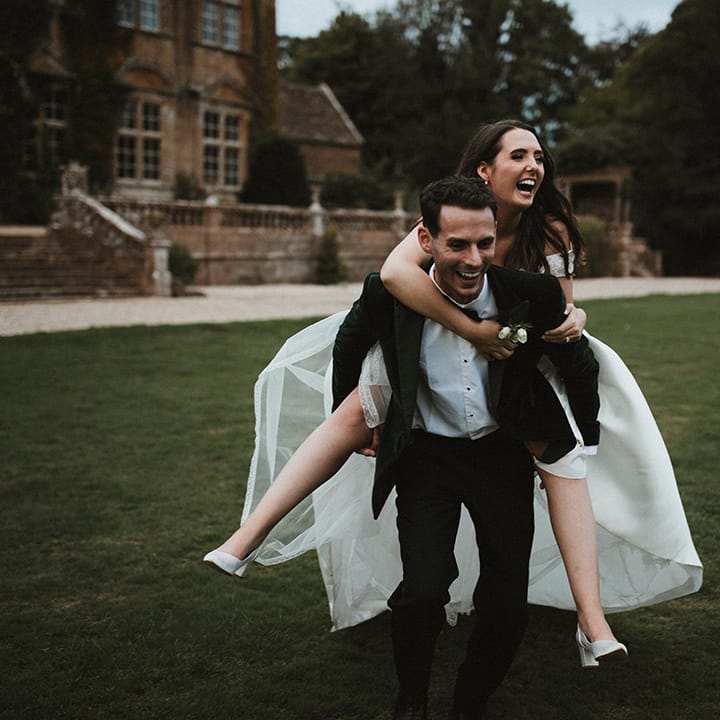 The groom lifts the bride onto his back as they pose for cute couple portraits 