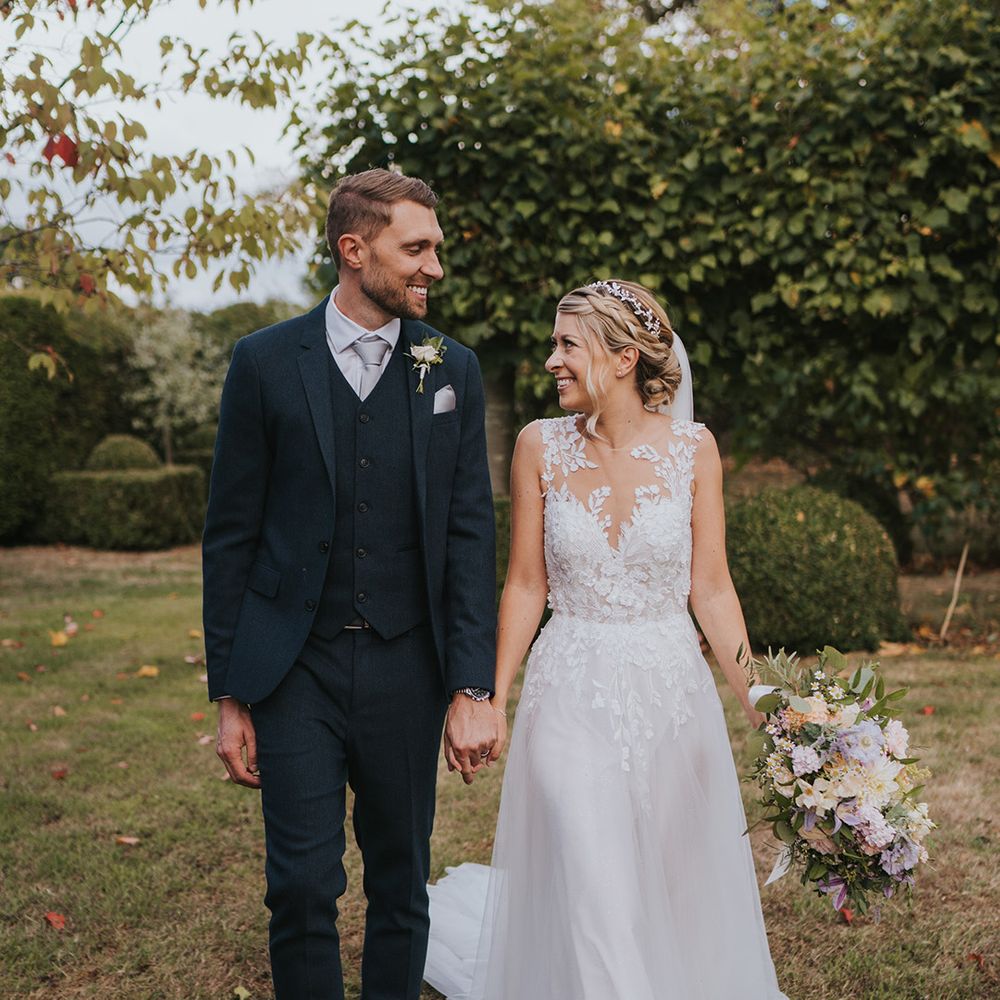 Groom smiling at the bride in a three piece navy suit and the bride in an illusion lace wedding dress with pretty pastel bouquet 