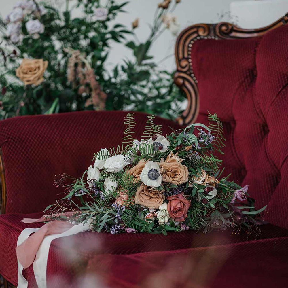 Dried wildflower bridal bouquet tied with neutral and dusky pink ribbon on maroon loveseat wedding furniture at Buxted Park 