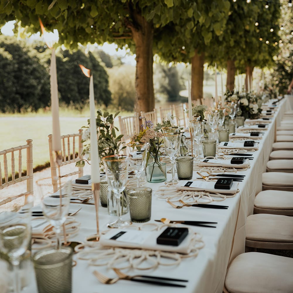 Gold rimmed wine glasses, green coloured glassware, white taper candles, with festoon lighting for outdoor wedding breakfast 