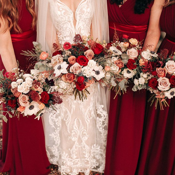 Bridal party wearing red bridesmaid dresses with the bride holding red rose and white anemone bouquet 