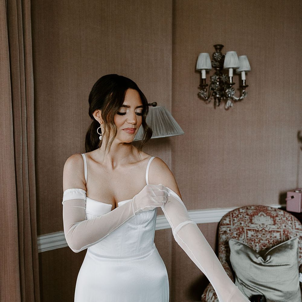 Bride putting on sheer bridal gloves to accessorise the Aleena Lena wedding dress 