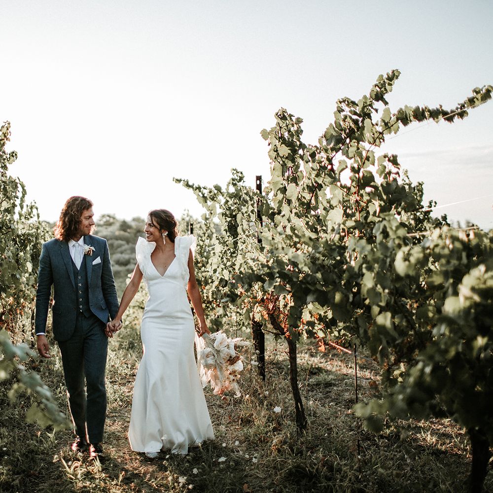 Groom in three-piece navy suit holding his brides hand in a plunging neckline Rime Arodaky wedding dress with ruffle sleeves 