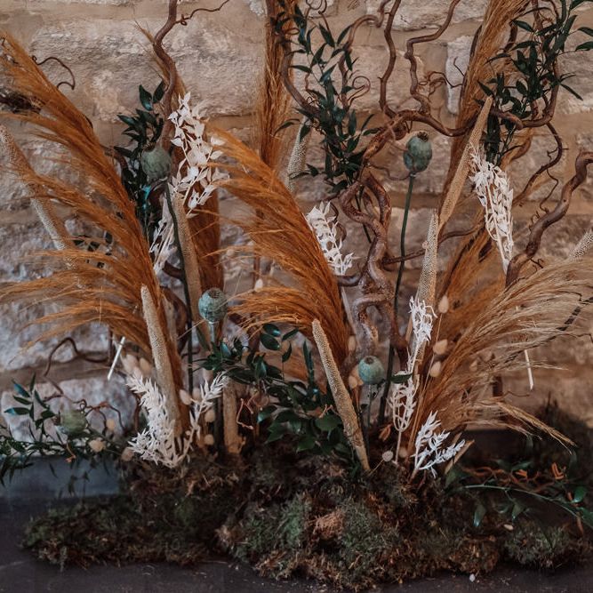Orange and green wedding floral arrangement with dried grasses, moss, foliage and poppy seeds