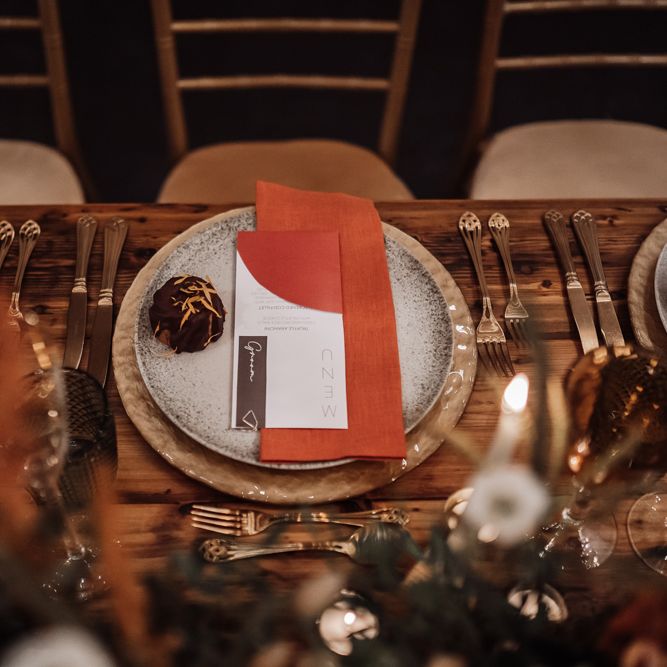 Place setting with gold charger plate and cutlery, patterned tableware and orange napkin 