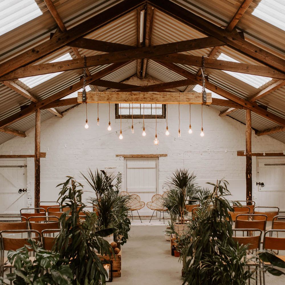 Tropical wedding theme at White Skye Barns with tropical plants and rattan chairs at the altar