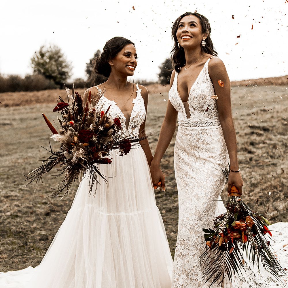 Confetti moment with two brides in a tulle and fitted lace wedding dress holding their orange and red flower bouquet 