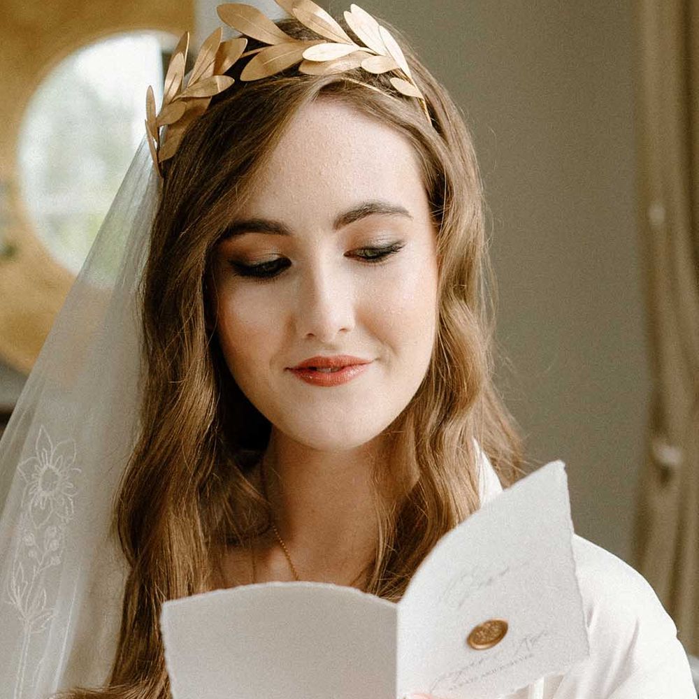 Wedding morning with bride with manicured nails reading a card with long wavy hair, lace veil and gold crown headdress 