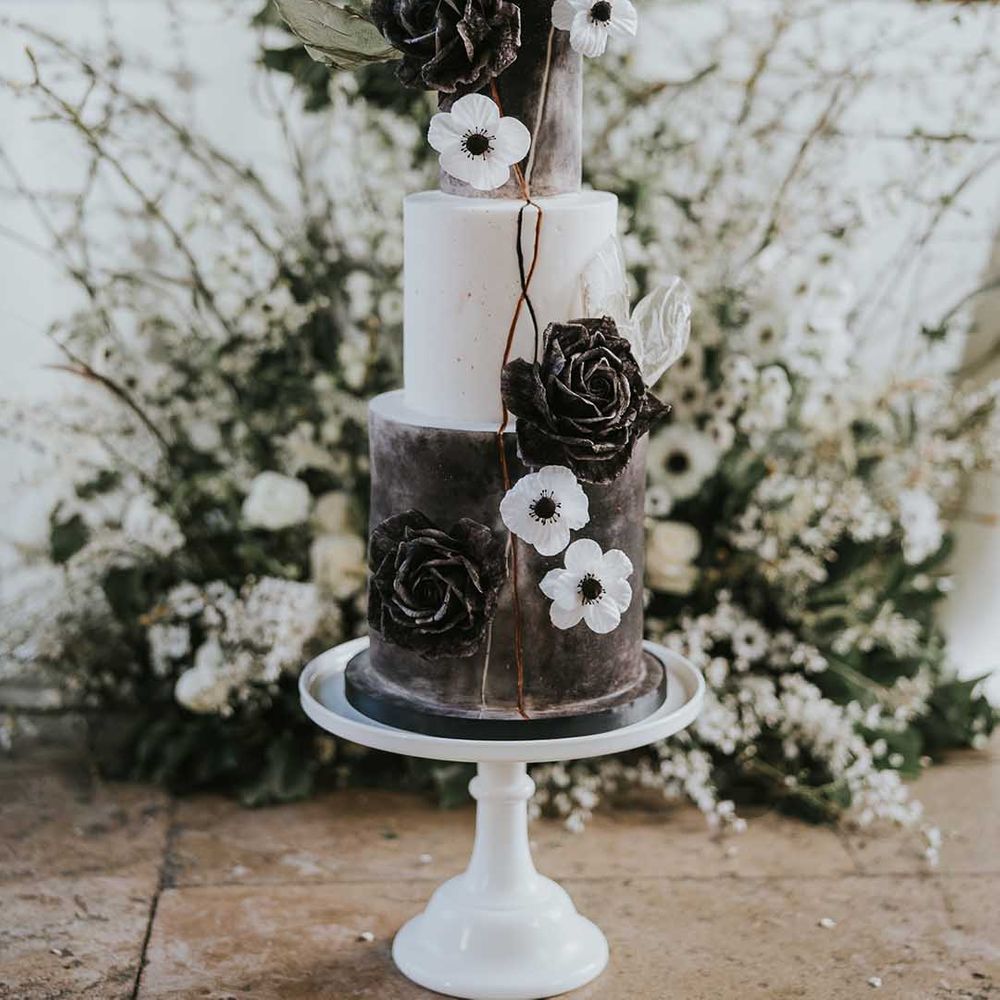 Monochrome wedding cake resting on the intimate reception table decorated with white flowers 