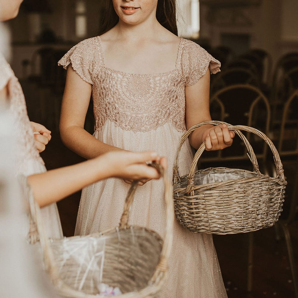 Flower girl wears neutral bridesmaids dresses and carries wicker basket