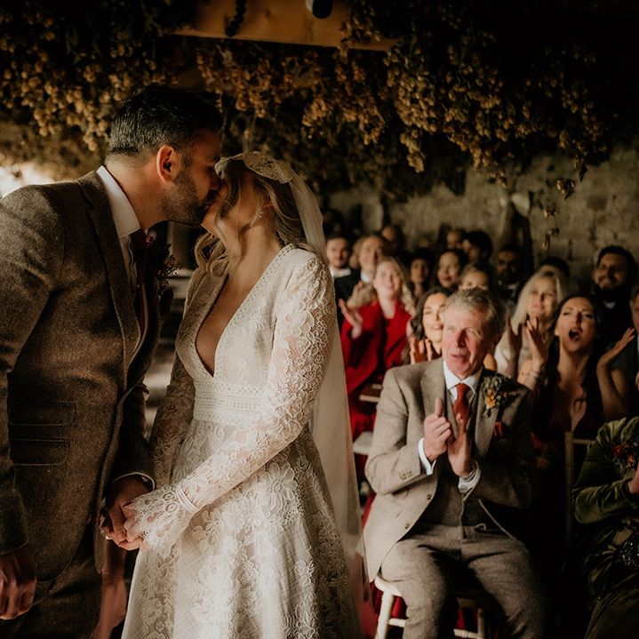 Groom in a wool suit and bride in lace dress kissing at their Lyde court wedding ceremony 