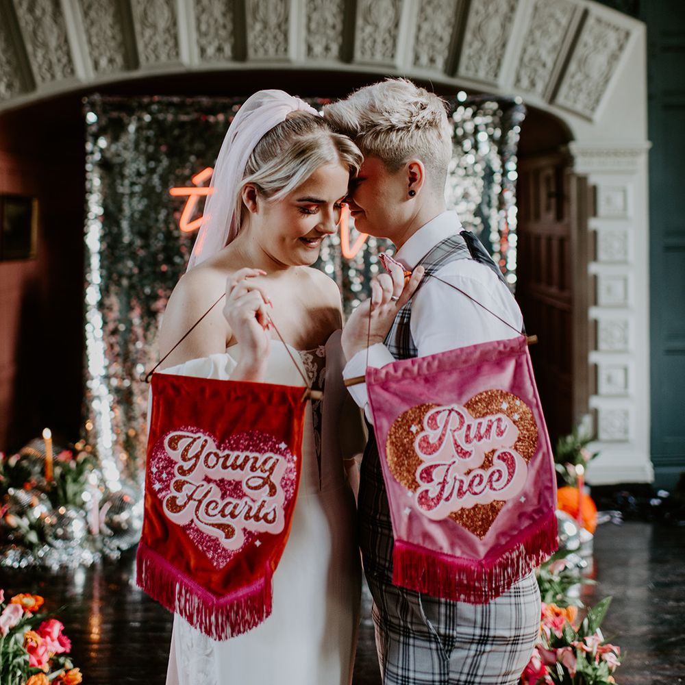 Two brides holding velvet fabric banners saying young hearts run free at fun retro wedding 
