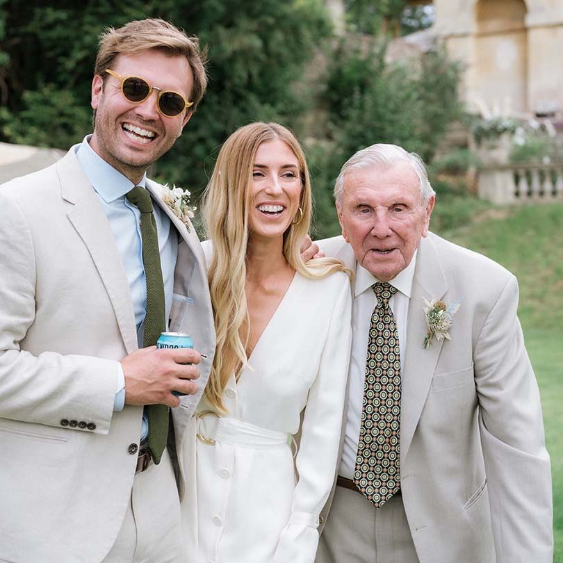 Bride and groom with guest in light coloured suit and green tie to match the colour scheme and dried flower buttonholes 