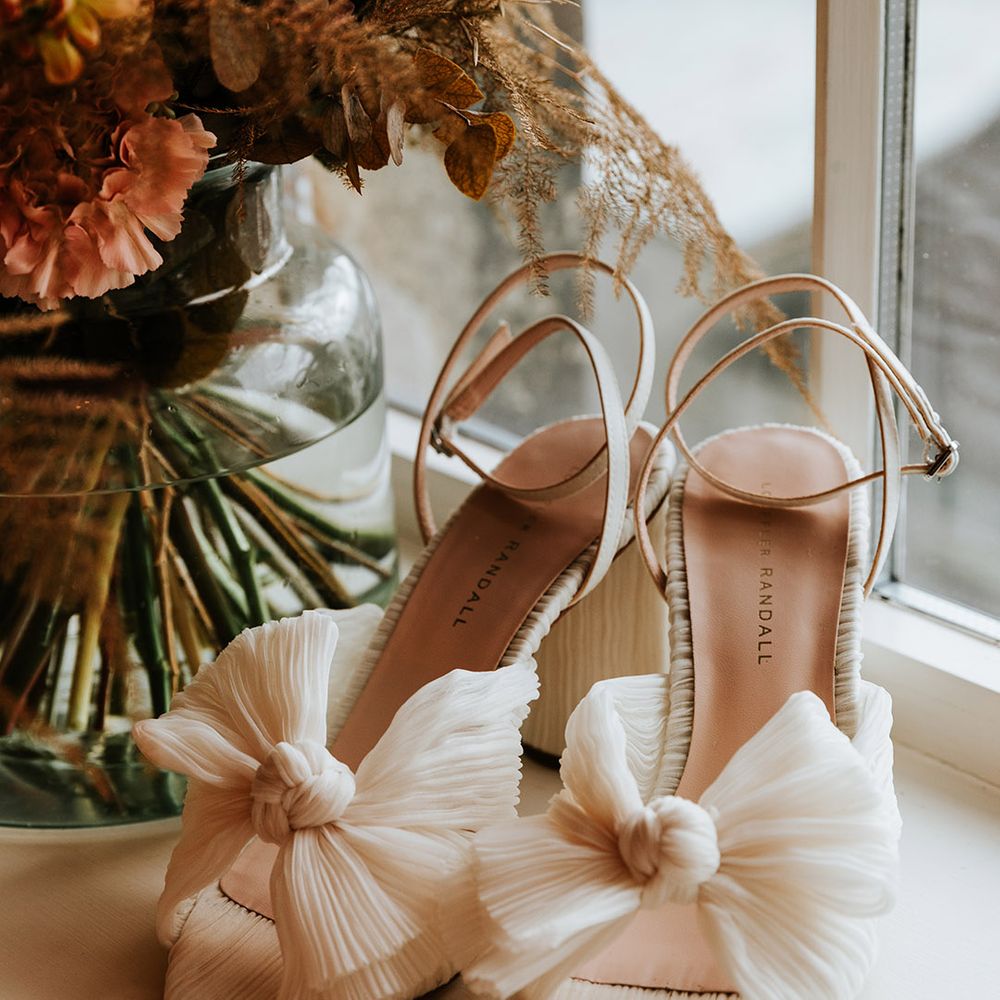 Loeffler Randall white bow wedding shoes next to vase of autumnal flowers 