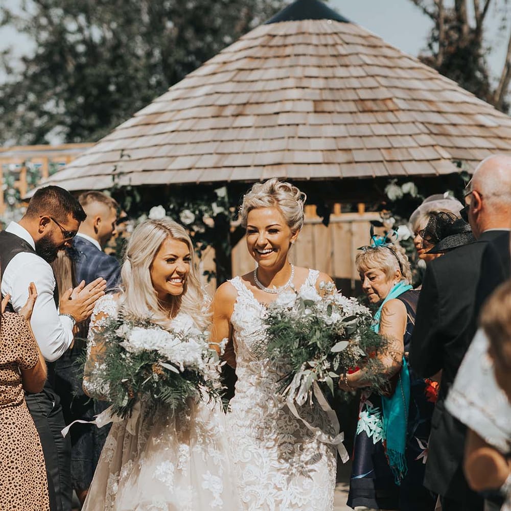 Newlyweds exit their outdoor LGBTQI+ wedding ceremony smiling and laughing