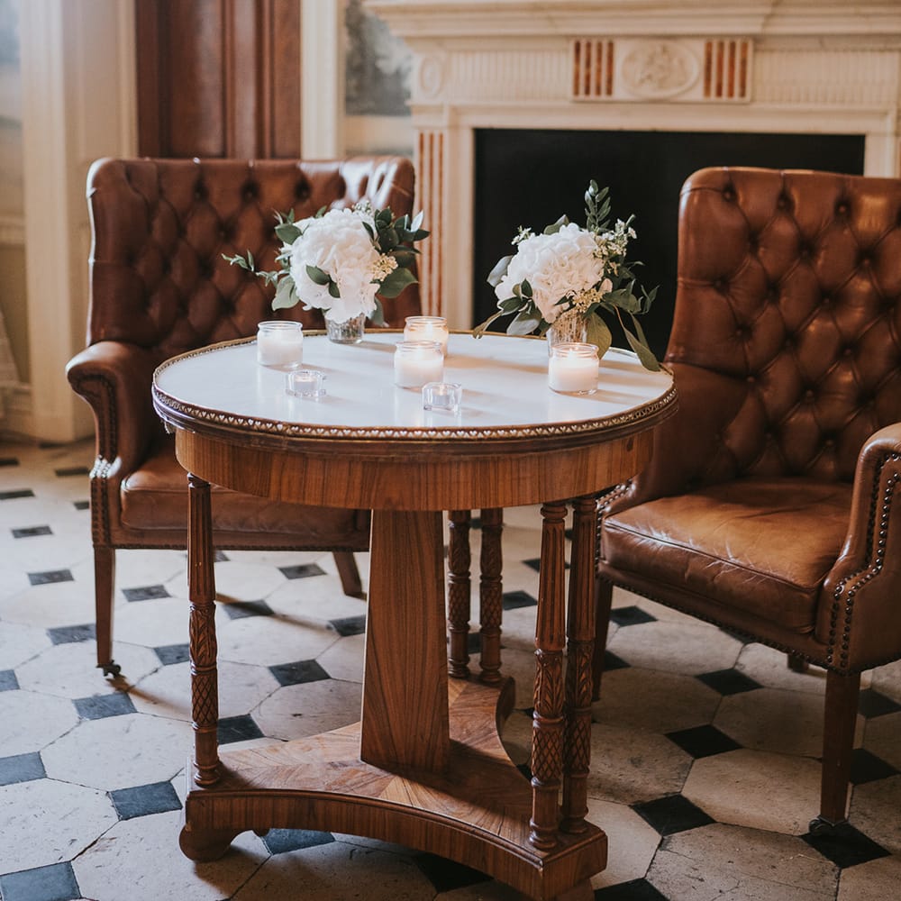 Candles and glass vase of white flowers with dark brown leather chairs 