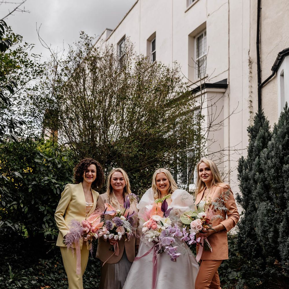 Bridal party in different coloured bridesmaid suits with the bride in a JESUS PEIRO wedding dress holding a tropical flower bouquet with orchids, anthuriums and astilbe 