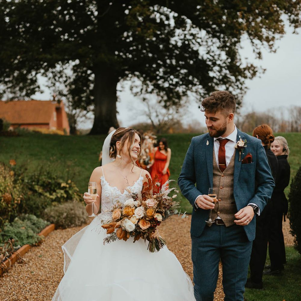 Bride and groom walk together after their wedding ceremony carrying a glass of Champagne 