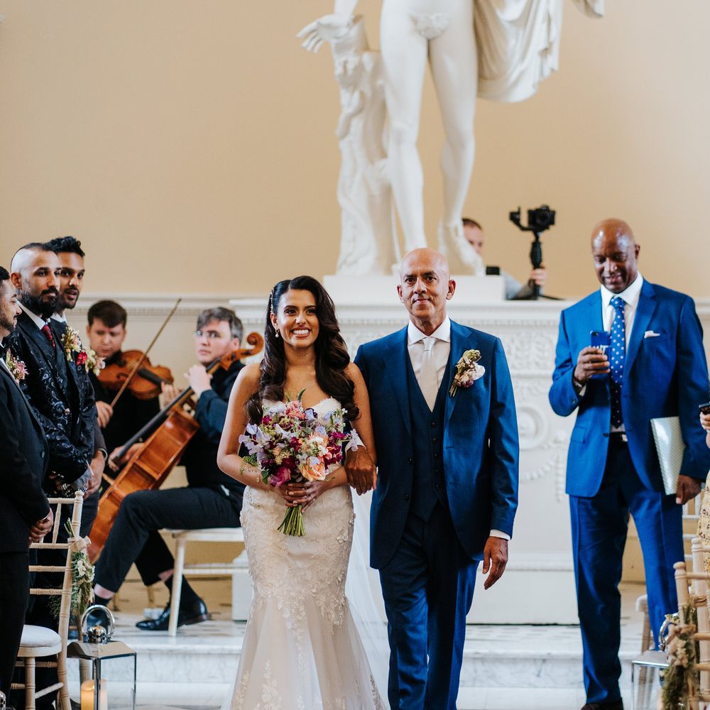 Bride wears lace fitted wedding dress and walks alongside her father as string quartet plays at Syon Park  