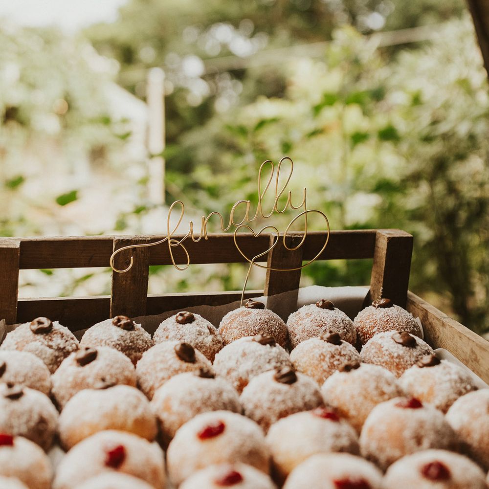 Filled doughnuts for the wedding favours with a wire cake topper saying 'finally' in a wooden crate box 