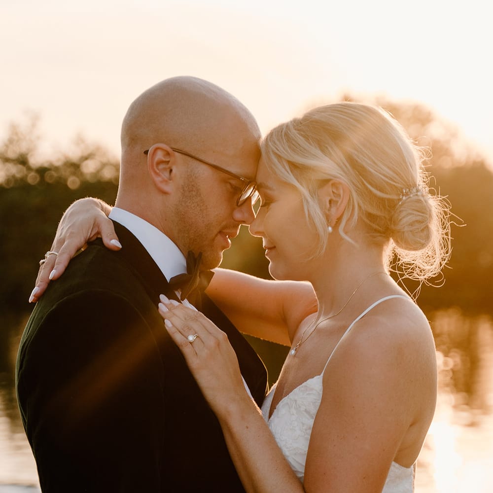 Bride wears her blonde hair in low up do and embraces her groom during golden hour