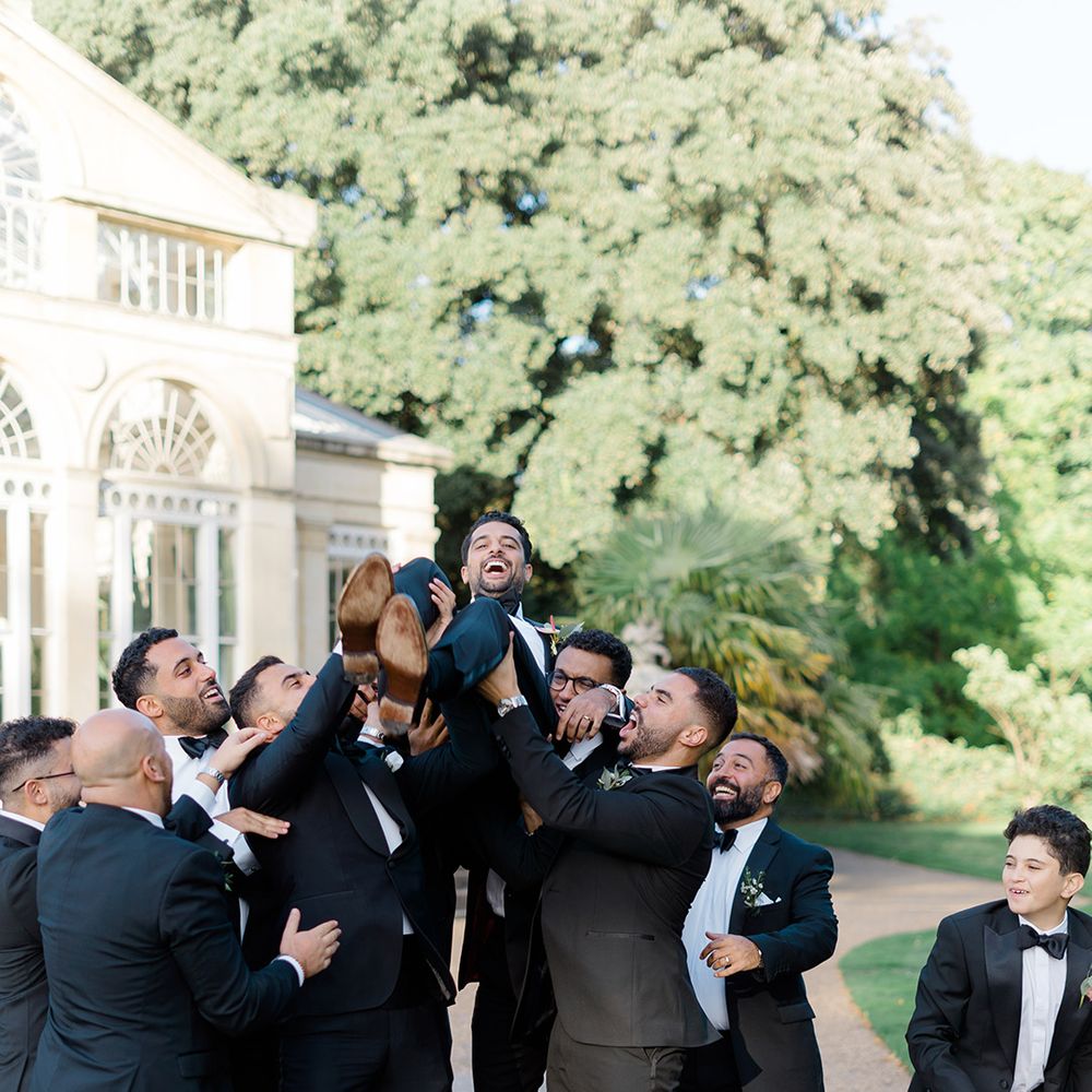 Groomsmen in black tie lift groom in the air outdoors 
