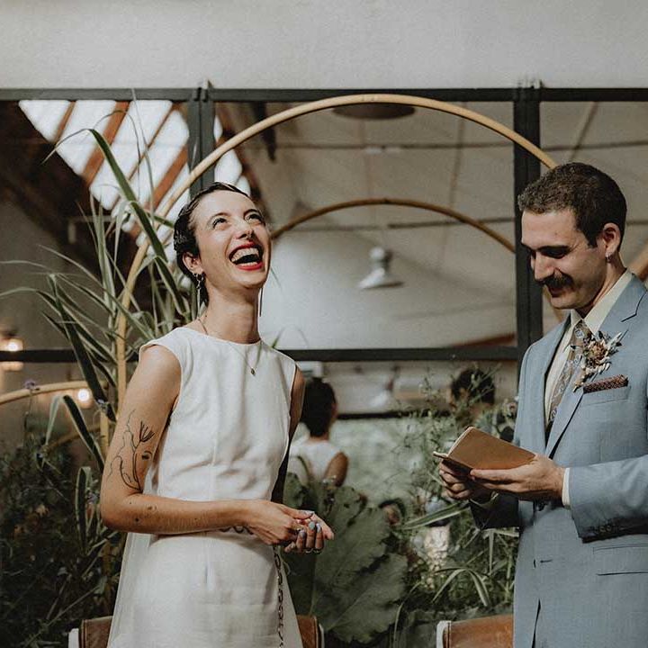Lisa in fitted pre loved wedding dress with bateau neckline laughs as Gabriel reads vows during non denominational wedding ceremony