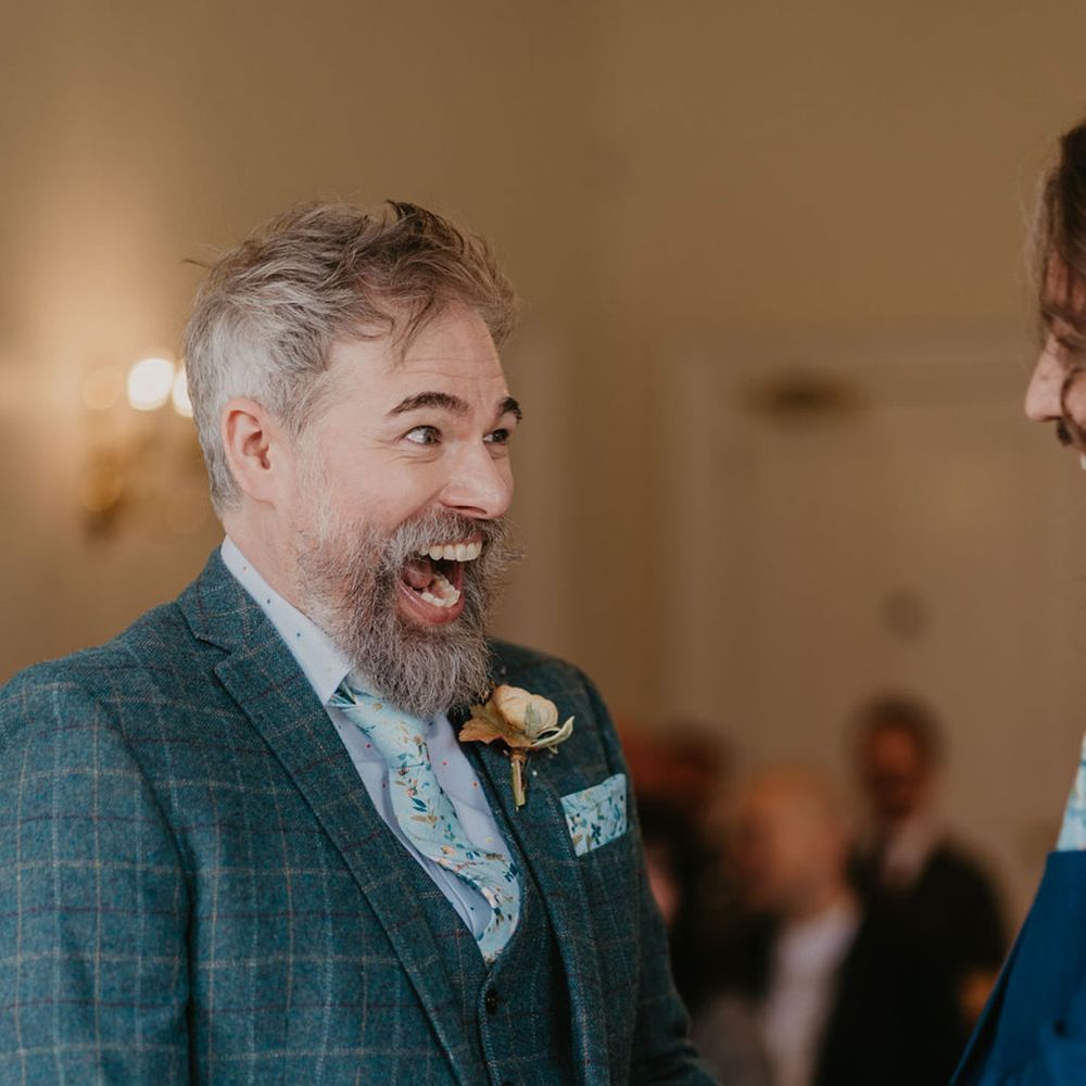 Groom wears three piece tartan suit complete with floral tie and matching pocket square alongside floral buttonhole 