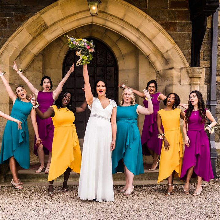 Bride stands with her bridesmaids who wear colourful bridesmaid dresses in purple, teal and yellow