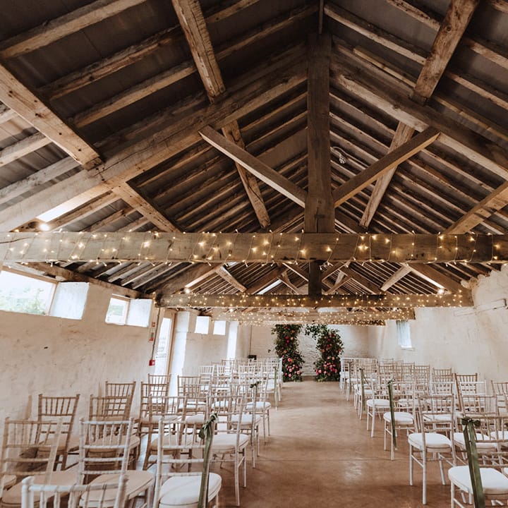 The Courtyard wedding venue in Shropshire with wooden beams, fairy lights and the altar decorated with big pink flower column arrangements