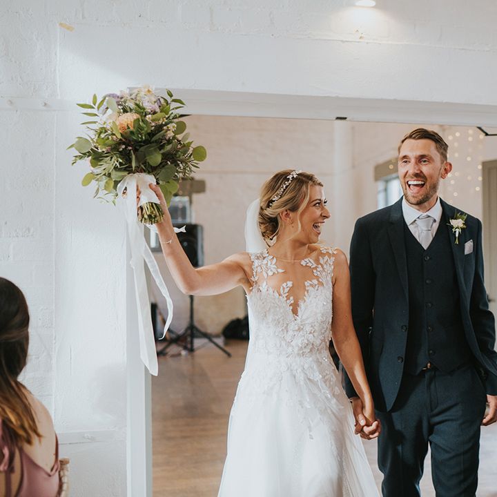 Bride in illusion lace Dando London wedding dress enters the wedding reception with the groom in a navy suit 