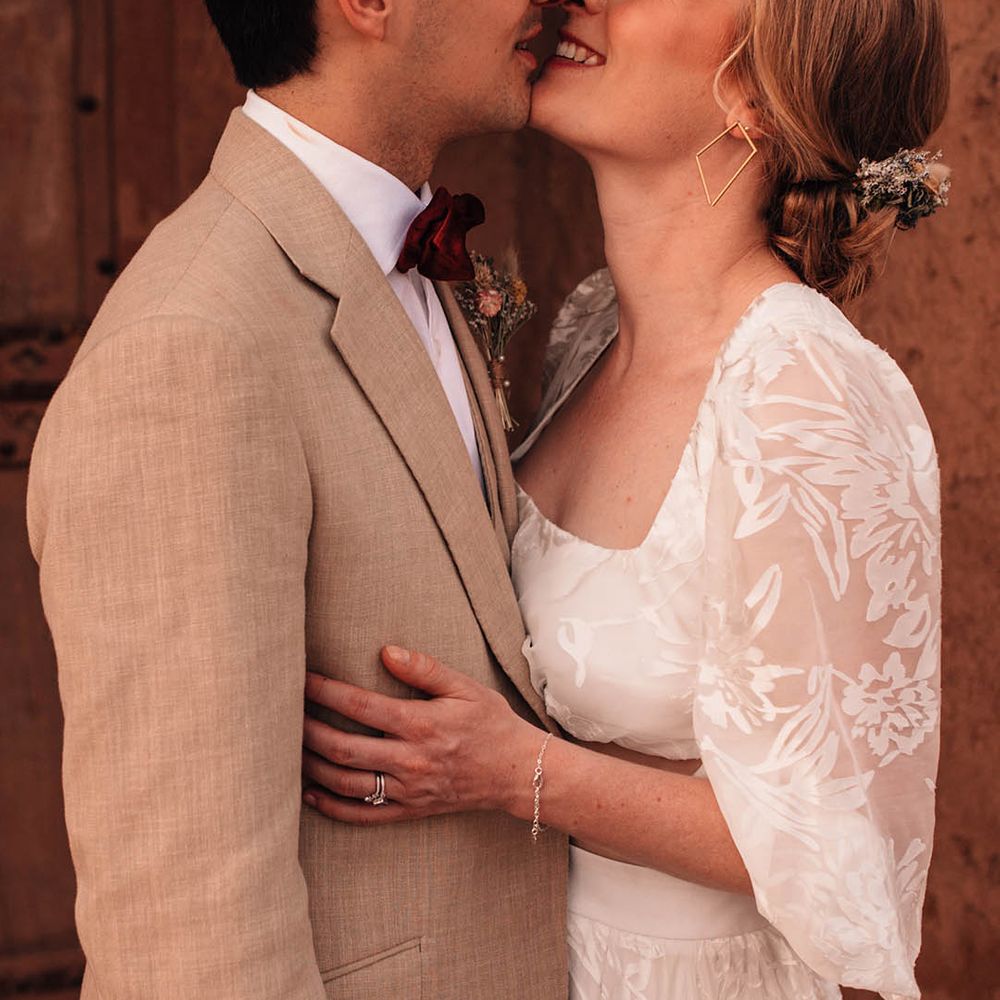 Bride in lace long sleeve crop top with the groom in cream suit leaning in for a kiss 