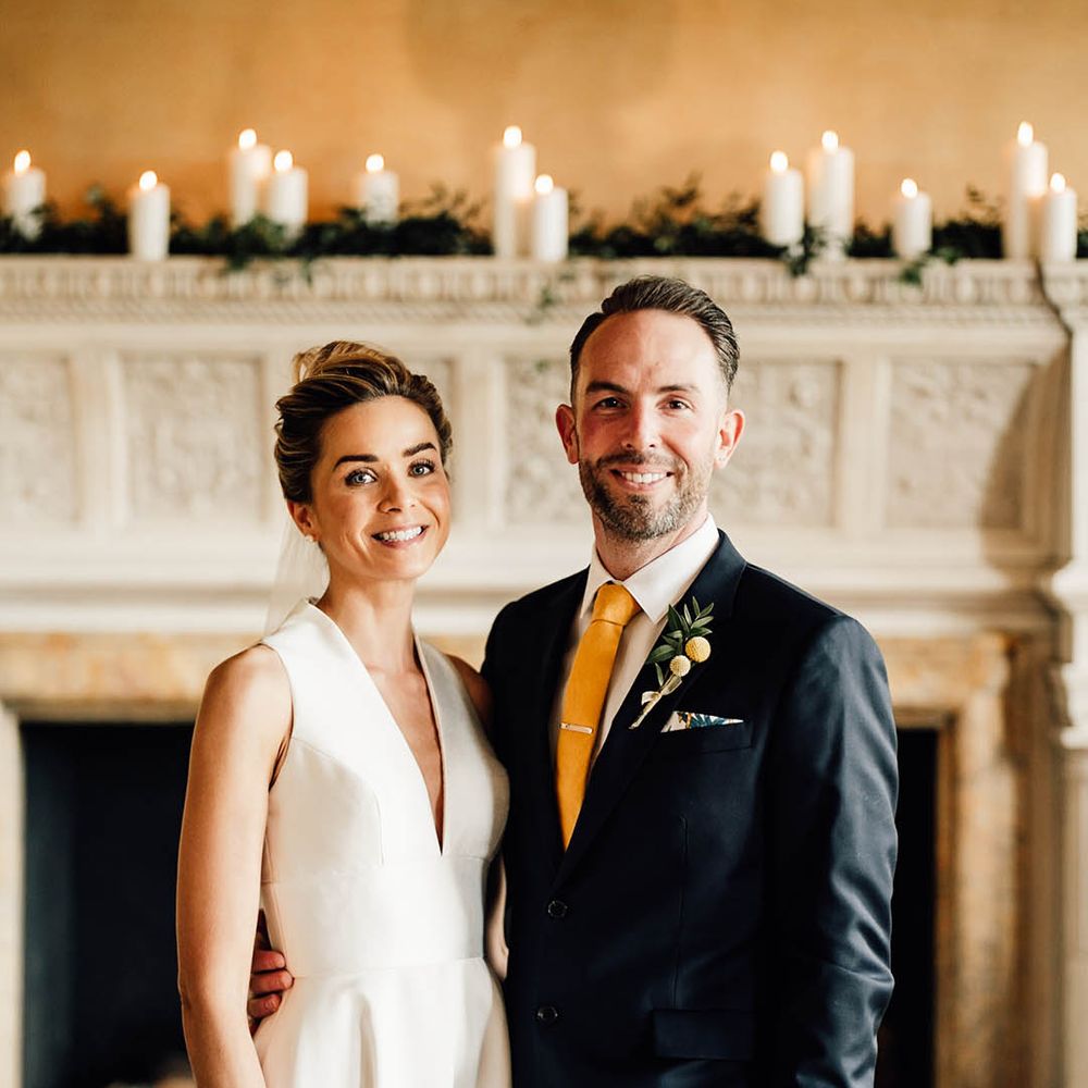 Bride in a plunging neckline Sheila Harding sleeveless wedding dress with the groom in a navy suit with yellow tie and buttonhole with tie clip 