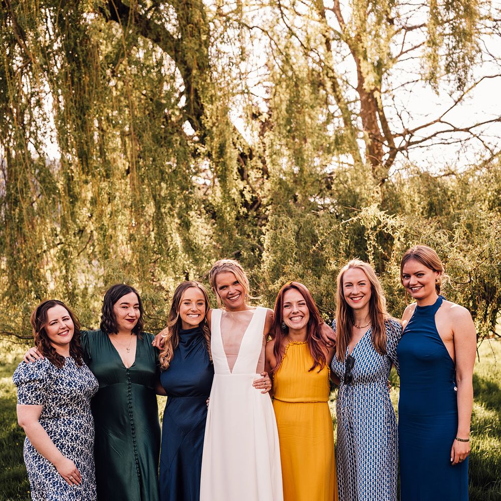 Bridesmaids in blue, yellow, and green mismatched bridesmaid dresses with the bride 