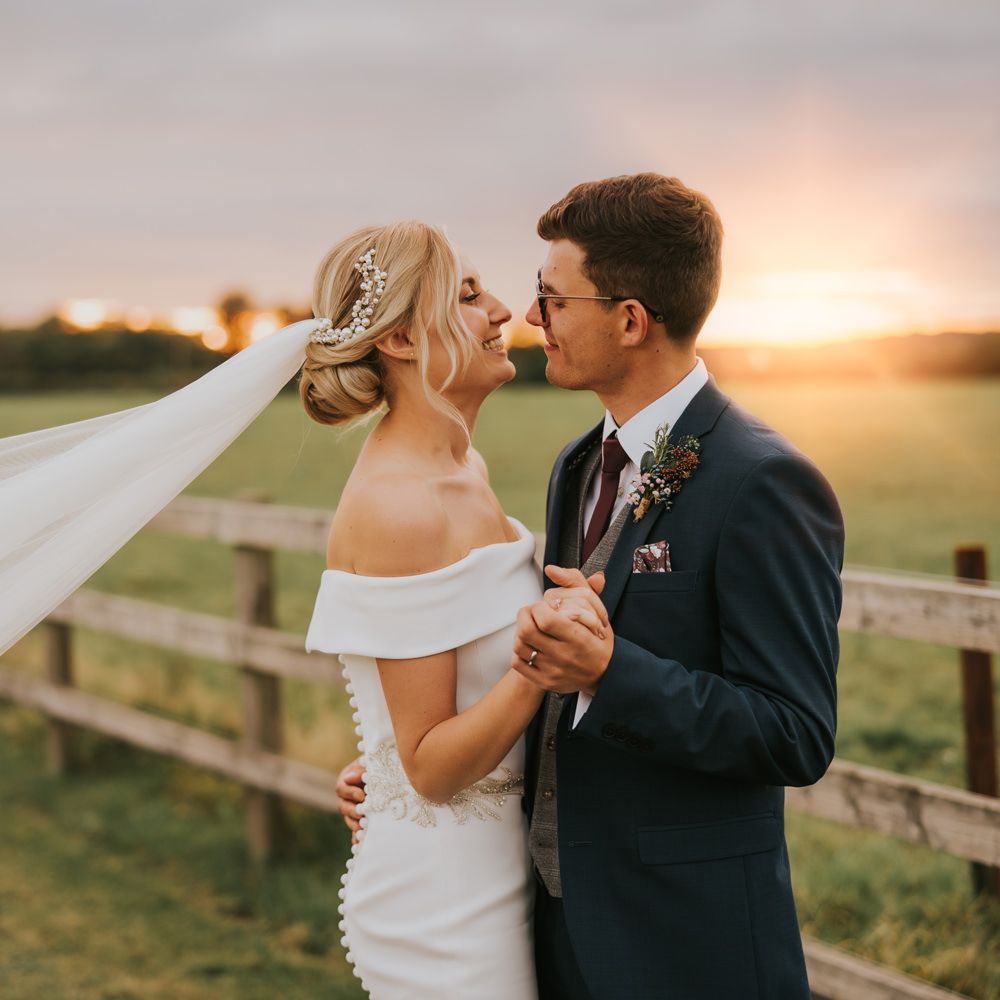 Bride & groom kiss as the sunsets and the brides veil blows in the wind
